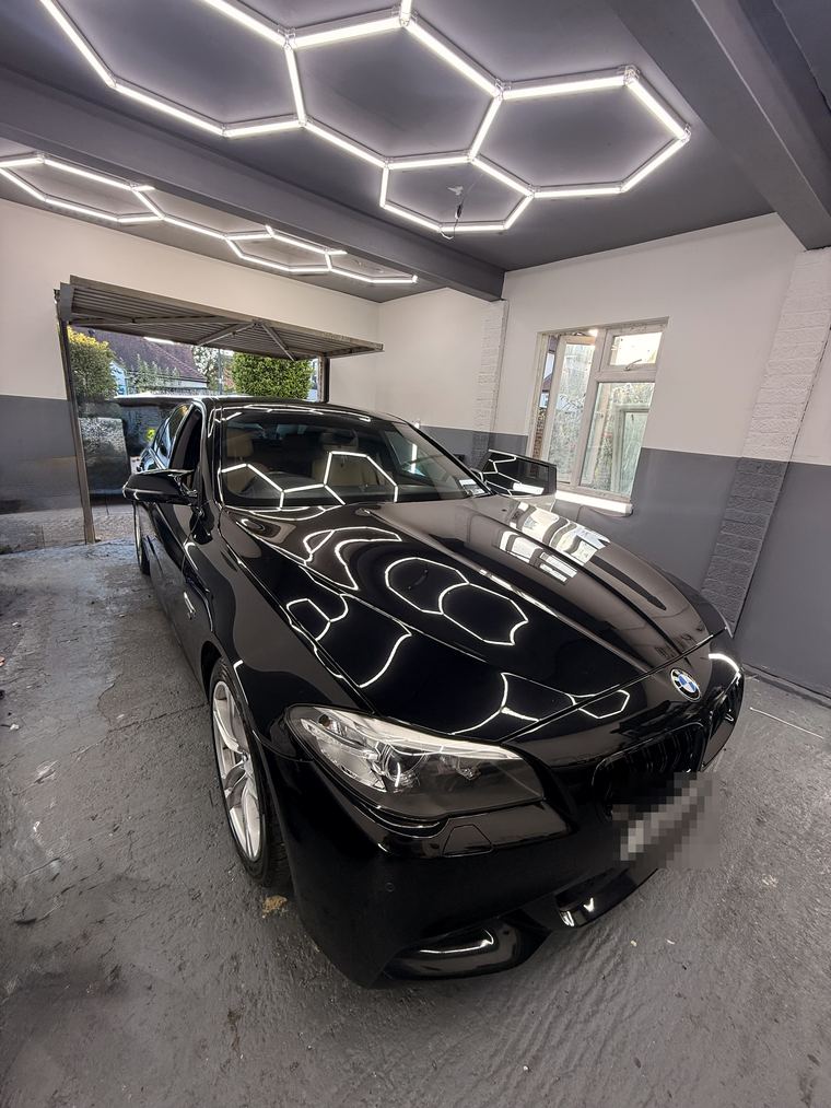 Black BMW 5 Series in the workshop bay, the hexagon ceiling lights reflected along its bonnet
