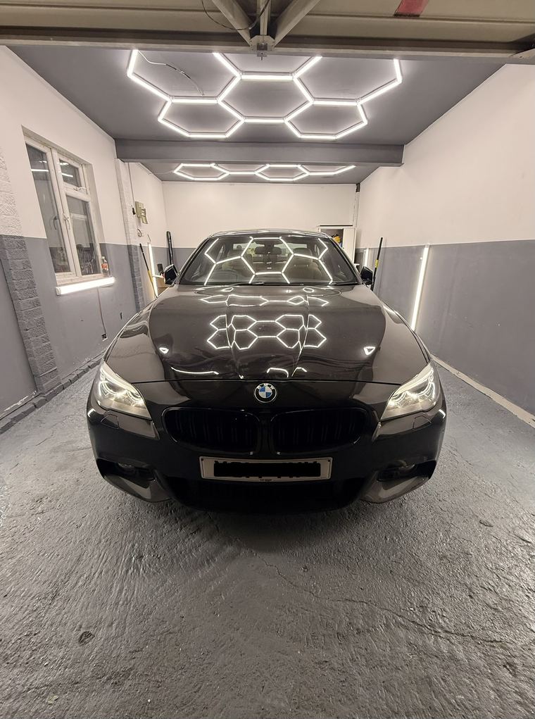 Black BMW 5 Series head-on under the hexagon lights, headlights on
